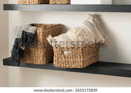 Wicker Storage Baskets with Knitted Pattern Cotton Blankets and Textured Pillow on Wooden Floating Shelves Set in a Naturally Lit Living Room with Beige Wall.