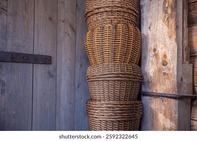 Wicker storage baskets on the background of wooden gates of a village house. Baskets stacked in front of the dark wooden walls of an old farmhouse. Traditions and culture of the villager.