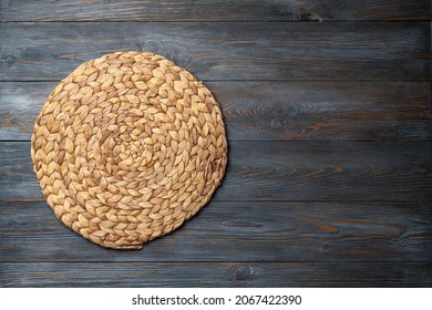 Wicker straw place mat on wooden dark background. Round woven straw mat on wooden gray dining table. Menu, dining, eating concept. Top view, copy space