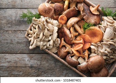 Wicker tray with variety of raw mushrooms on wooden table