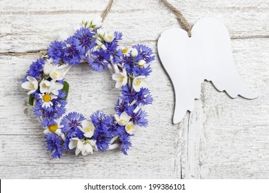 Wicker wreath decorated with cornflowers and chamomiles, and wooden angel wings - Powered by Shutterstock