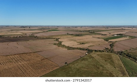 Wide aerial drone shot of patchwork agricultural fields and farmlands under a clear blue sky in Entre Rios, Argentina.