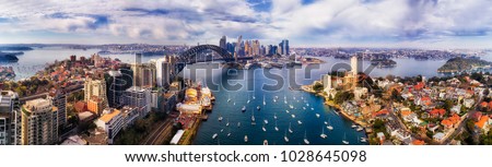 Wide aerial panorama of Sydney city CBD landmarks on shores of Sydney Harbour from Lower North Shore to distant Barangaroo.