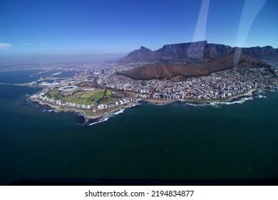 Wide Aerial View Over Cape Town With Blue Sea, Coast Line Stadium Sea Point And Clifton In The Foreground And Lions Head, Table Mountain City And Harbour In The Back, Blue Sky Sunlight