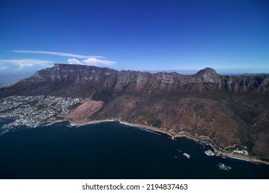 Wide Angel Aerial View Of Rocky Coast Line From Camps Bay Cape Town Along The 12 Apostles And Table Mountain View, Blue Sea And Blue Sky