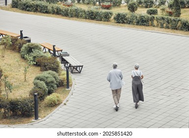 Wide angle back view at contemporary mature couple riding electric scooters in park, copy space