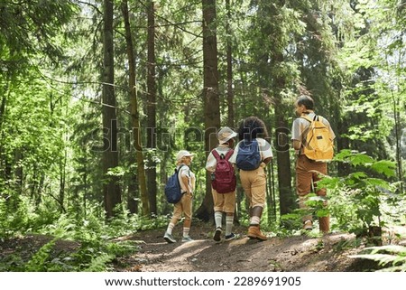 Wide angle back view at diverse group of scouts hiking in forest with adult leader, copy space