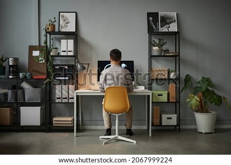 Wide angle back view at man using computer at home office with modern tech interior, copy space