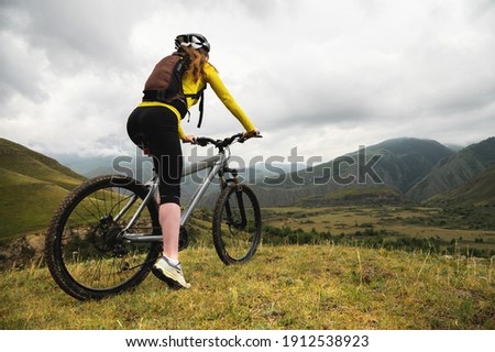 Wide angle bottom view of a young woman sitting on a mountain bike high in the mountains against the backdrop of epic rocks in the evening. Mountain sports bike
