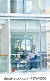 Wide Angle Of Business Meeting In Modern Office Behind Glass Windows, Shot From Outside Building