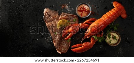Wide angle of delicious red lobster and beef steak as a surf and turf, served with lemon and herbs near sauces with spices on black background