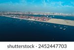 A wide angle drone view of Karachi port with city scape at the back and blue water in front. Import export terminal is visible with fishing boats. 