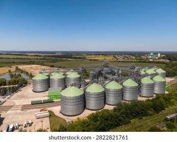 Wide angle elevated perspective of comprehensive agroindustrial storage facility featuring massive metallic grain silos in rural landscape under clear sky.