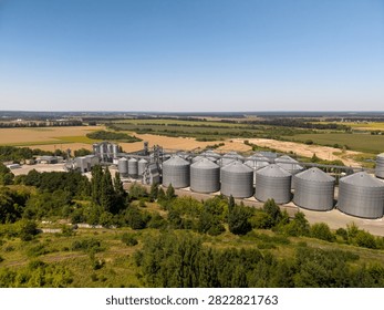 Wide angle elevated perspective of large scale industrial agricultural storage terminal situated in countryside rural landscape under clear sky.