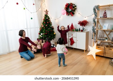 Wide Angle Of Happy Asian Mother And Kids Playing With Balloons In A Festive Living Room Decorated For Christmas At Home