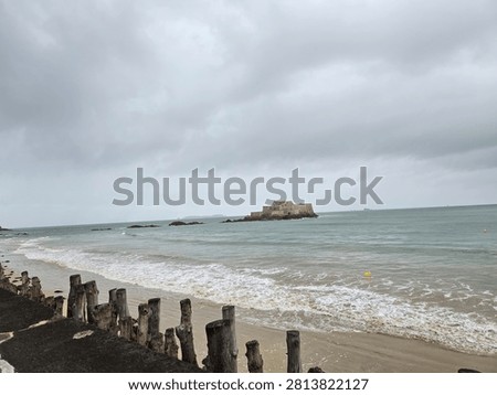 Wide angle horizontal view of weathered wooden breakwater posts on a sandy beach under an overcast sky in Saint-Malo, Brittany, France, for travel tourism and moody web banner background copy space.