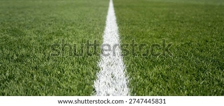 A wide angle low perspective shot of a straight white line painted on a vibrant green grass field for sports competition.
