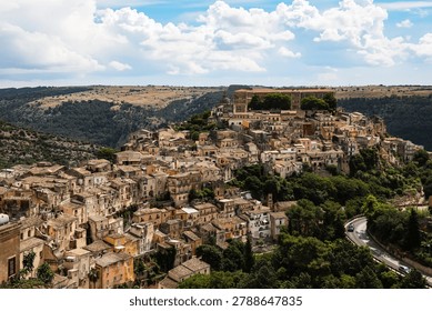 Wide angle panoramic view of the ancient hilltop town of Ragusa Ibla in Sicily Italy featuring old stone houses and baroque buildings clustered together on the mountain slope under a dramatic sky