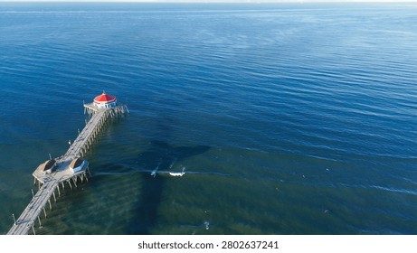Wide angle perspective of pier reaching into calm Pacific ocean provides serene focal point. Soft morning sunlight creates vast, tranquil sea horizon, highlighting natural beauty of CA coastline. USA