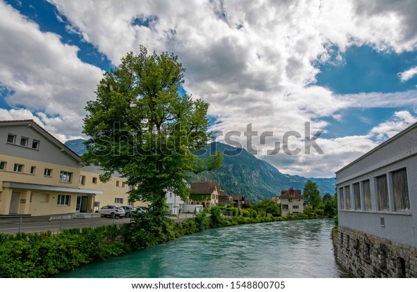 Wide angle perspective view of Aare\
River with turquoise water in Interlaken, Switzerland with Swiss\
Alps on background under the dramatic cloudy\
sky