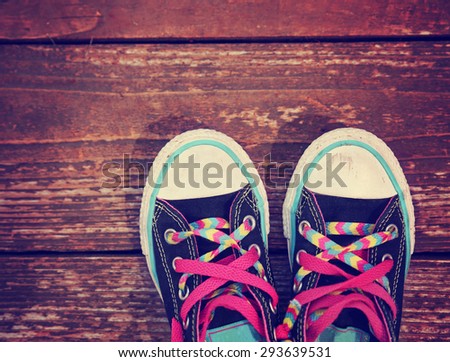 a wide angle photo of a pair of generic looking shoes like converse sneakers with pink shoe laces on a vintage wooden background toned with a retro vintage instagram filter app