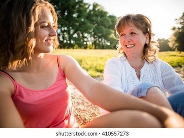 Wide angle photo of teen girl with her mature mother talking together, outdoor in nature