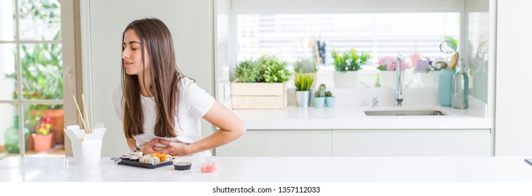 Wide Angle Picture Of Beautiful Young Woman Eating Asian Sushi From Delivery With Hand On Stomach Because Indigestion, Painful Illness Feeling Unwell. Ache Concept.