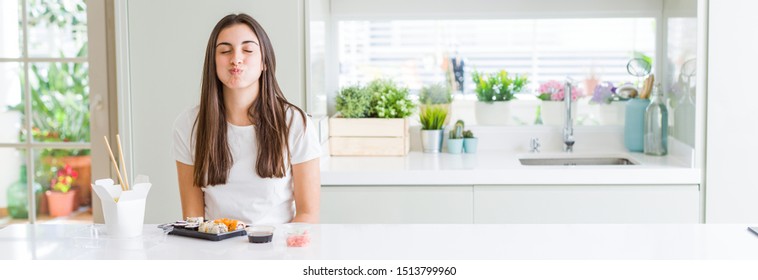 Wide angle picture of beautiful young woman eating asian sushi from delivery puffing cheeks with funny face. Mouth inflated with air, crazy expression.