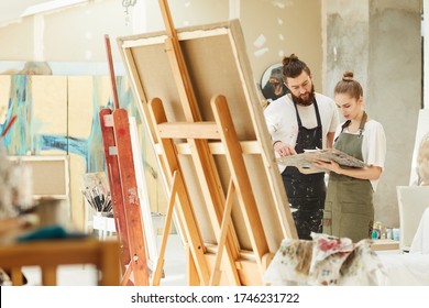 Wide Angle Portrait Of Creative Couple Painting Picture Together While Standing By Easel In Art Studio Interior, Copy Space