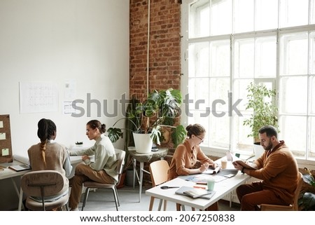Wide angle portrait of diverse creative team working in modern studio lit by sunlight, copy space
