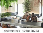 Wide angle portrait of two contemporary men collaborating on project during business meeting in green office or cafe interior, copy space