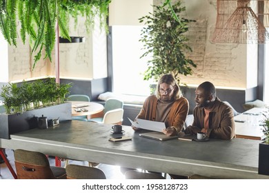 Wide Angle Portrait Of Two Contemporary Men Collaborating On Project During Business Meeting In Green Office Or Cafe Interior, Copy Space