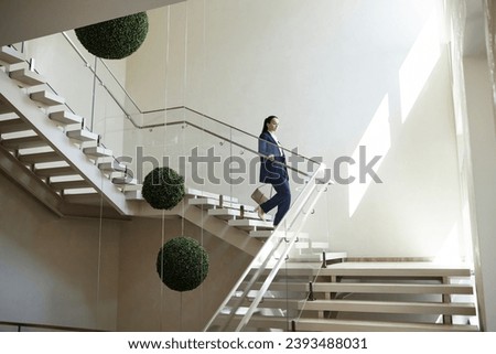 Wide angle shot of Caucasian woman in business suit carrying purse going downstairs holding on handrail in modern office building, copy space