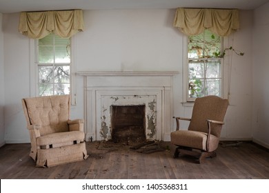 Wide Angle Shot Of Dramatic Living Room With Two Lonely Chairs And A Fireplace In An Abandoned Home During The Day In The Deep Rural South