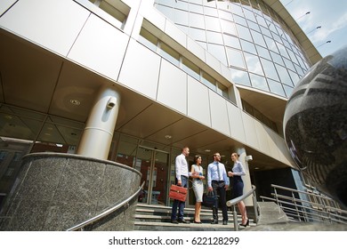 Wide Angle Shot, Group Of Business People Standing On Steps Of Modern Office Building With Glass Fronts