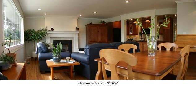 A wide angle shot of a modern great room consisting of a dining table, couches, fireplace, and a kitchen in the background