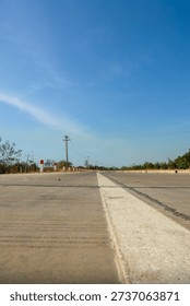 Wide angle shot of a new, empty concrete road extending into the distant horizon under a bright sunny blue sky, conveying travel and future opportunities.