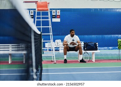 Wide angle shot of professional black sportsman sitting on bench in tennis court and holding water bottle, copy space - Powered by Shutterstock