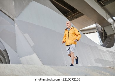 Wide Angle Shot Of Senior Man Running Outdoors In Urban City Setttting Against Concrete Background