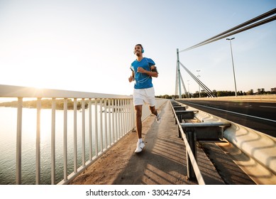 Wide Angle Shot Of Smiling Man Running On The Bridge Along A River. Warm Tones, Lens Flare.