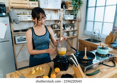 Wide Angle Shot Of A Sportive Korean Female Putting Orange Pulps Into The Blender While Making Juice In The Kitchen At Home After Morning Workout.