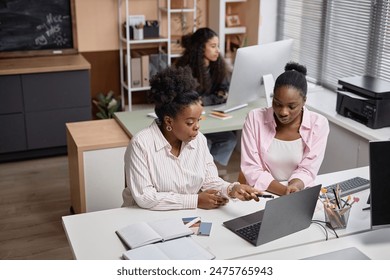 Wide angle shot of two African American women discussing business issues pointing at laptop screen in class or office, copy space - Powered by Shutterstock