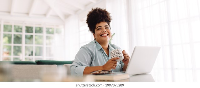 Wide Angle Shot Of Woman Sitting On Table With Coffee Mug And Laptop. Woman Taking Break While Working From Home.