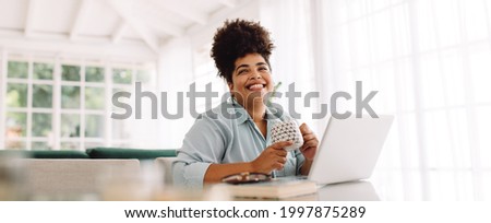 Wide angle shot of woman sitting on table with coffee mug and laptop. Woman taking break while working from home.