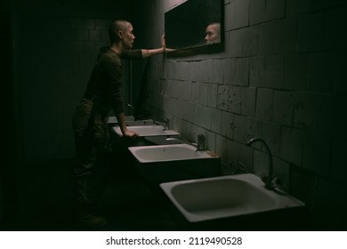 Wide Angle Side View At Tough Woman With Buzzcut Looking At Mirror In Dark Survival Setting, Copy Space