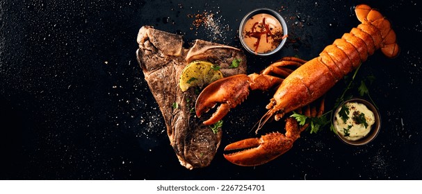 Wide angle top view of whole lobster served on beef steak with spices and lemon slices placed near sauces against black surface