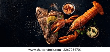 Wide angle top view of whole lobster served on beef steak with spices and lemon slices placed near sauces against black surface