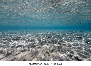 Wide Angle Underwater Scenic Of Shallow Clear Turquoise Water With Ripples Of Sunlight On A Rocky Ocean Floor. Red Sea, Egypt.