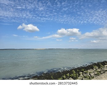 Wide angle view of altocumulus clouds over the open sea and seaweed covered rocky shoreline in Normandy, France, for travel, nature backgrounds, and coastal banner copy space.