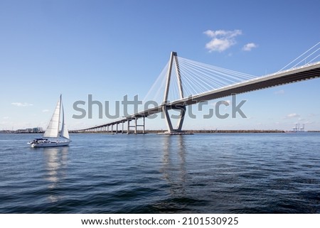 Wide angle view of Arthur Ravenel Jr. Bridge in Charleston, South Carolina, with a large sailboat floating by on a blue sky sunny day.